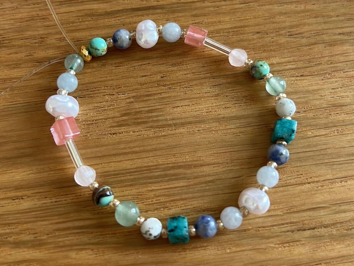 Armband aus bunten Steinperlen, Süßwasserperlen und Glasstäbchen in Türkis, Rosa und Blau auf Holz