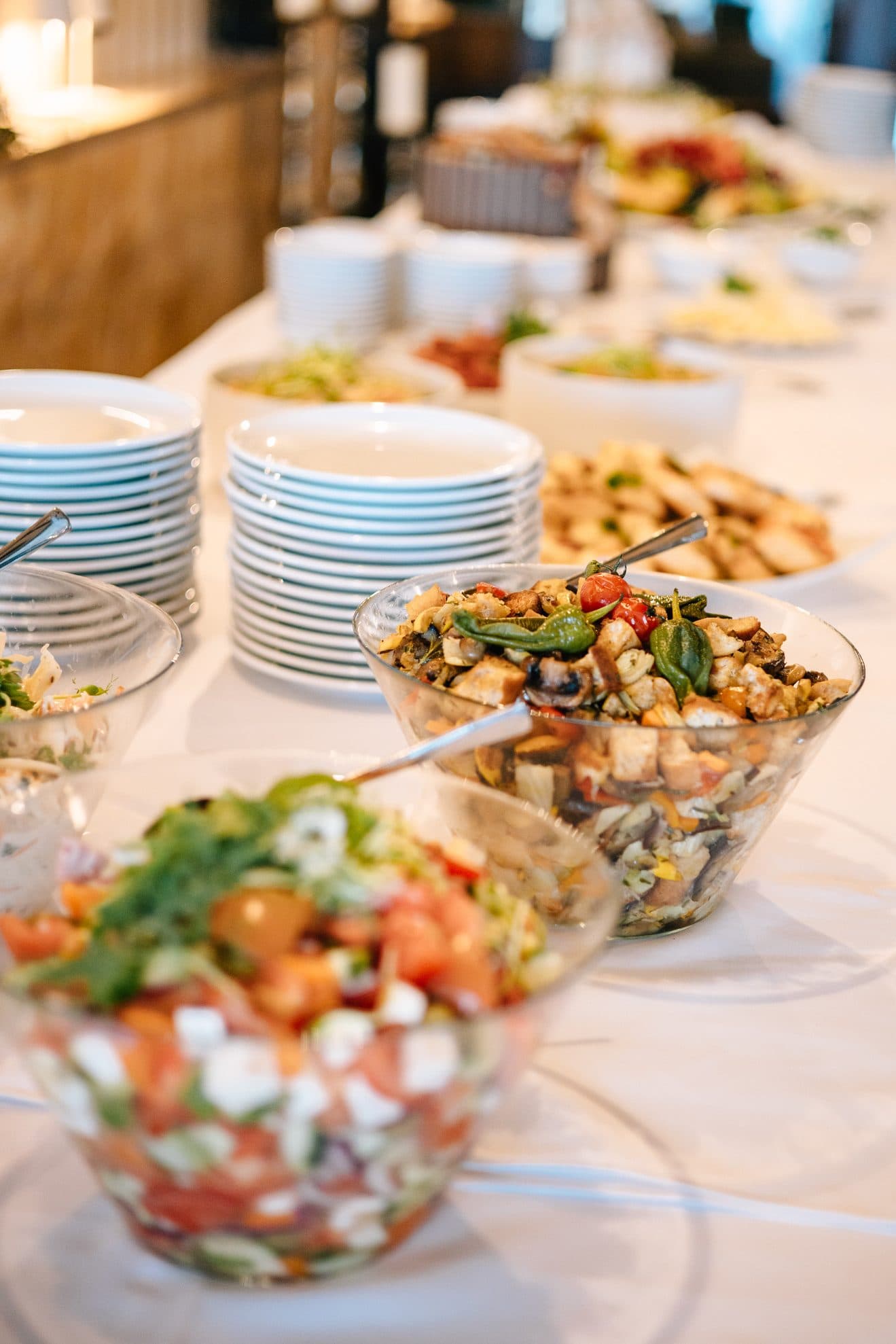 Salatbuffet mit gemischten Salaten in Glasschüsseln und gestapelten Tellern