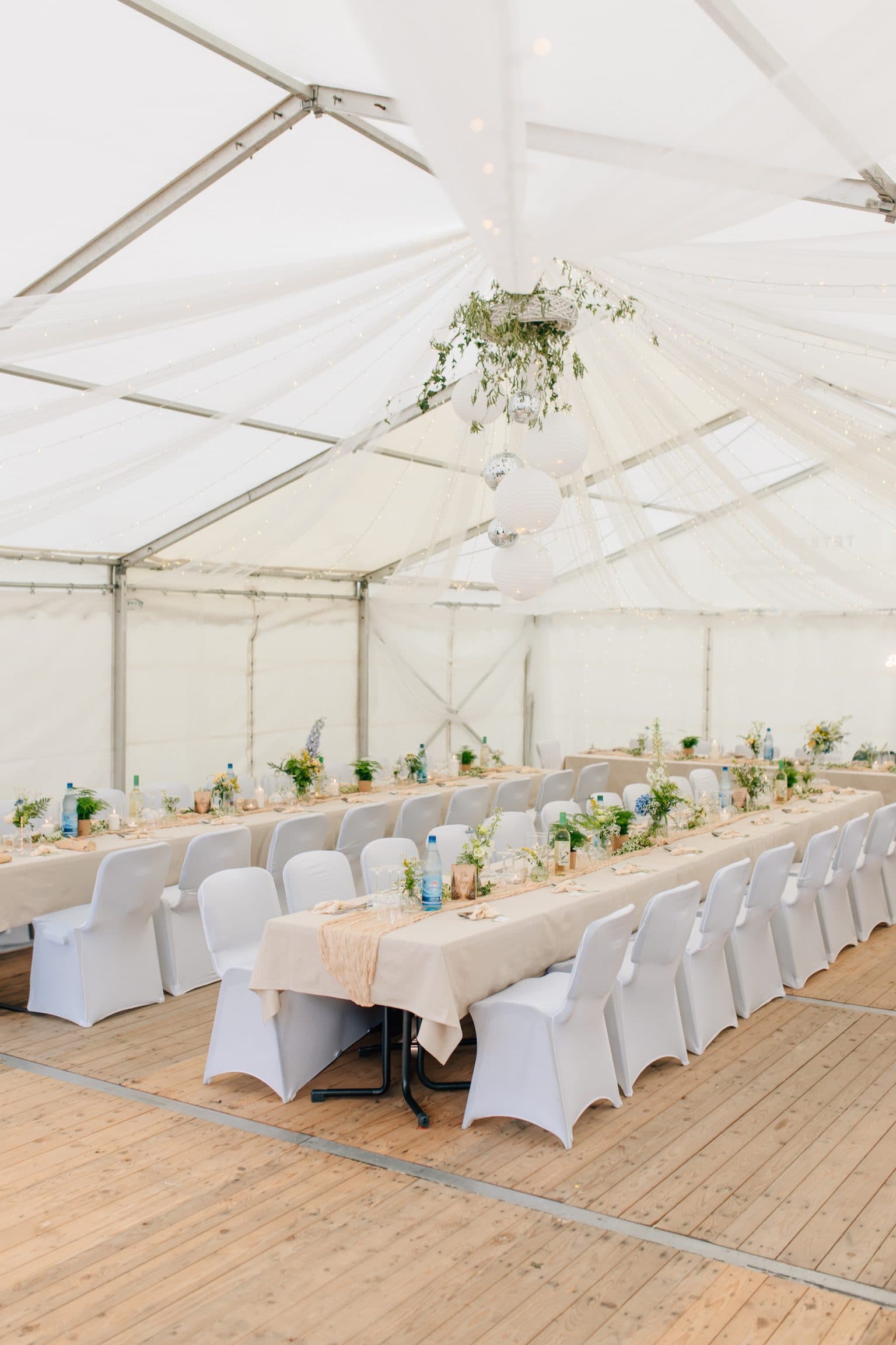 Festzelt mit gedeckten Tafeln, weißen Stuhlhussen und hängender Blumendekoration