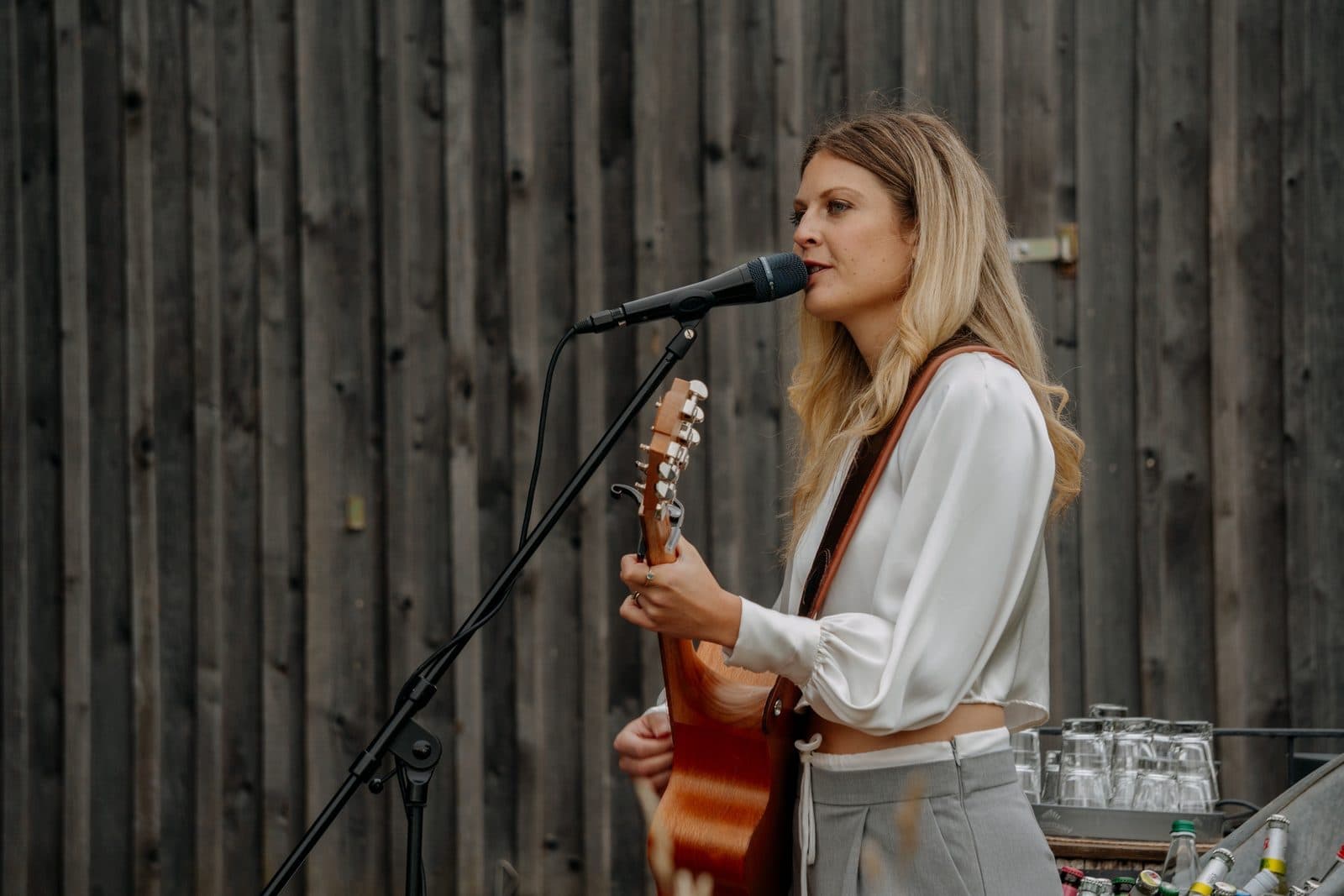 Luise Liebisch singt und spielt Akustikgitarre am Mikrofon vor dunkler Holzwand