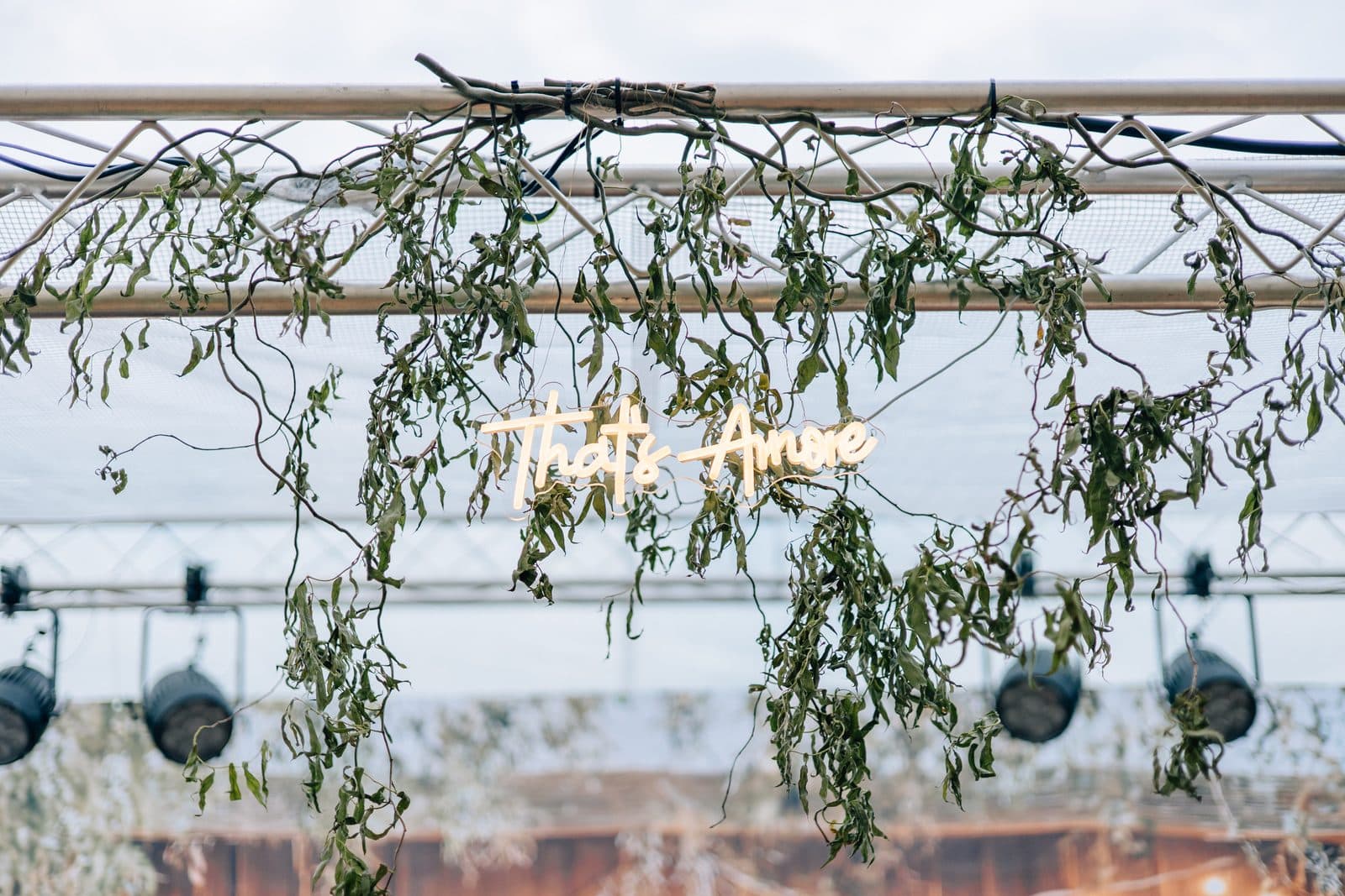 Neonschriftzug „That's Amore“ zwischen hängenden Weidenzweigen unter der Zeltkonstruktion