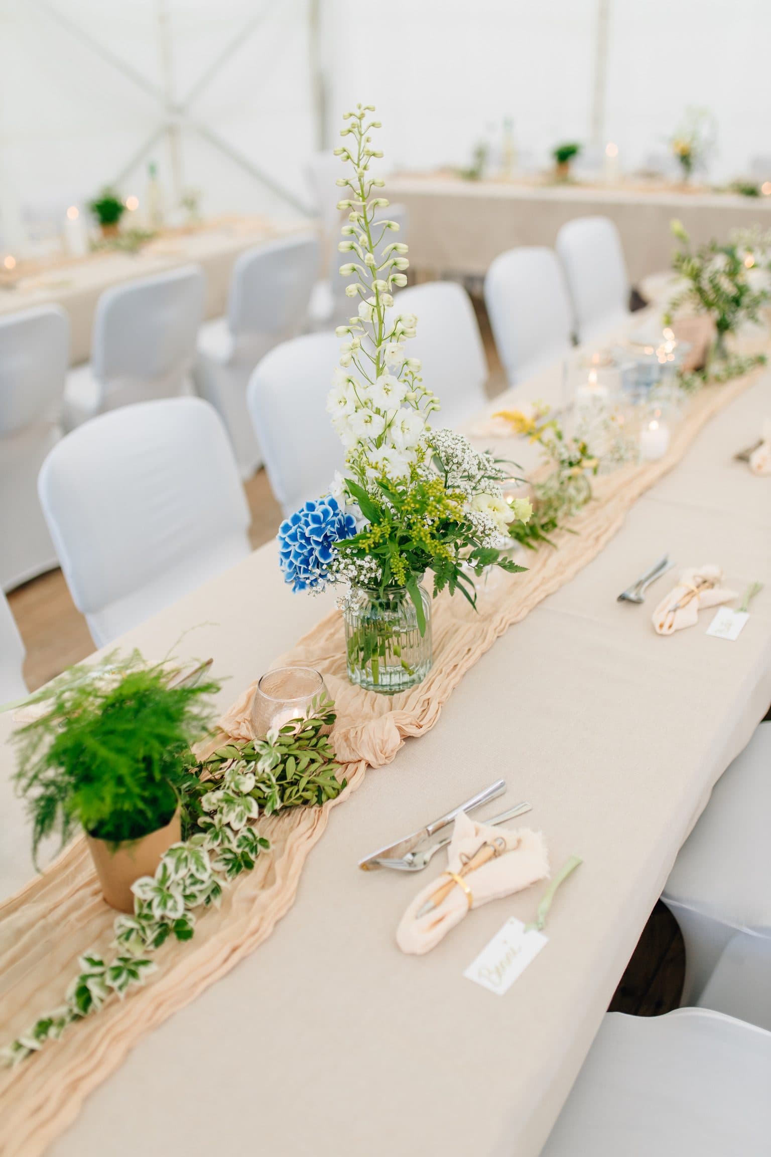 Gedeckte Festtafel mit Blumengesteck, Farn und Servietten mit Namenskärtchen