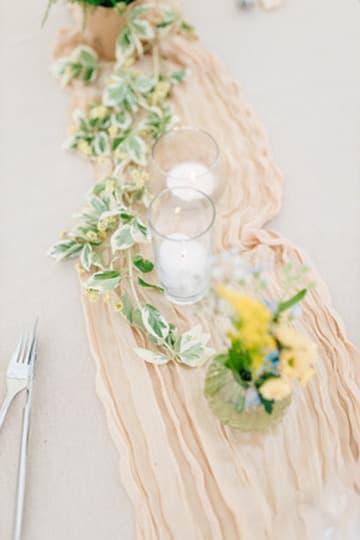 Detailaufnahme: Tischläufer in Beige mit Efeu, Kerzen und gelben Blüten