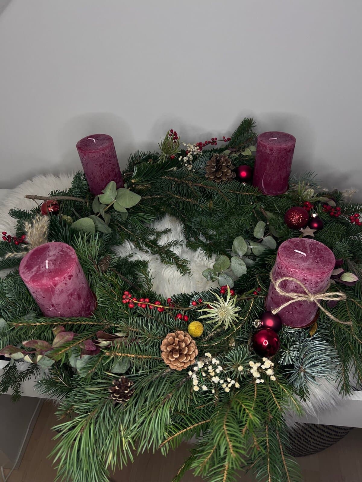 Handgebundener Adventskranz aus Tanne und Eukalyptus mit vier beerenroten Kerzen, Zapfen, Beeren, Christbaumkugeln und Jutebändchen