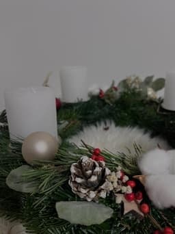 Detail eines Adventskranzes mit weißen Kerzen, beschneitem Zapfen, roten Beeren, Baumwollzweigen und Kugel