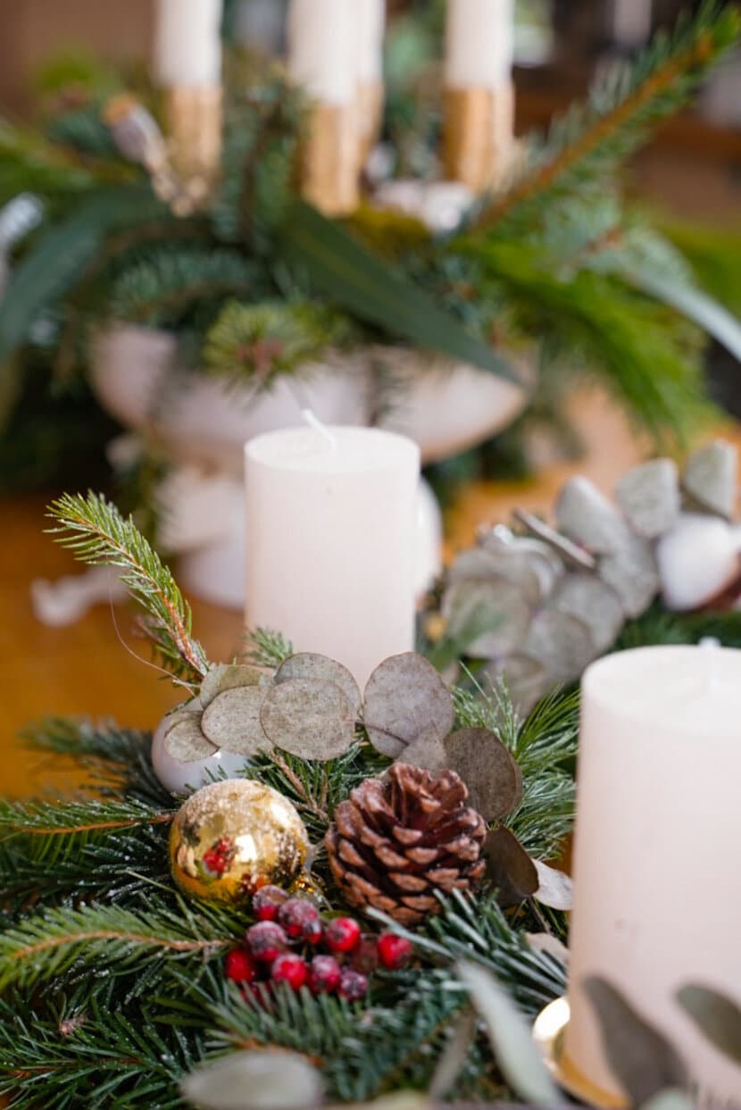 Detail eines Adventskranzes mit Zapfen, goldener Kugel, roten Beeren, Eukalyptus und weißen Kerzen
