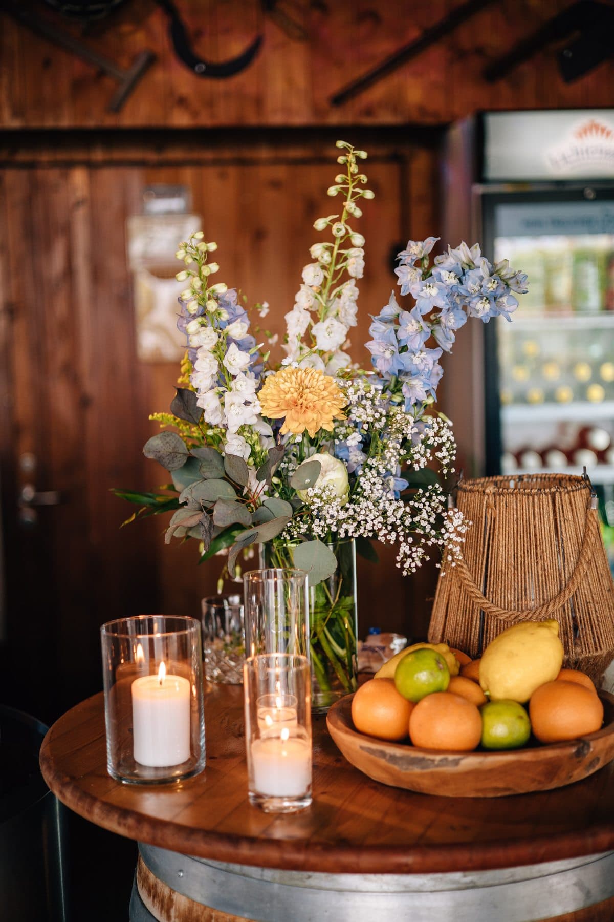 Hoher Blumenstrauß mit Rittersporn, Schleierkraut und gelber Chrysantheme, daneben Windlichter und eine Schale mit Zitrusfrüchten