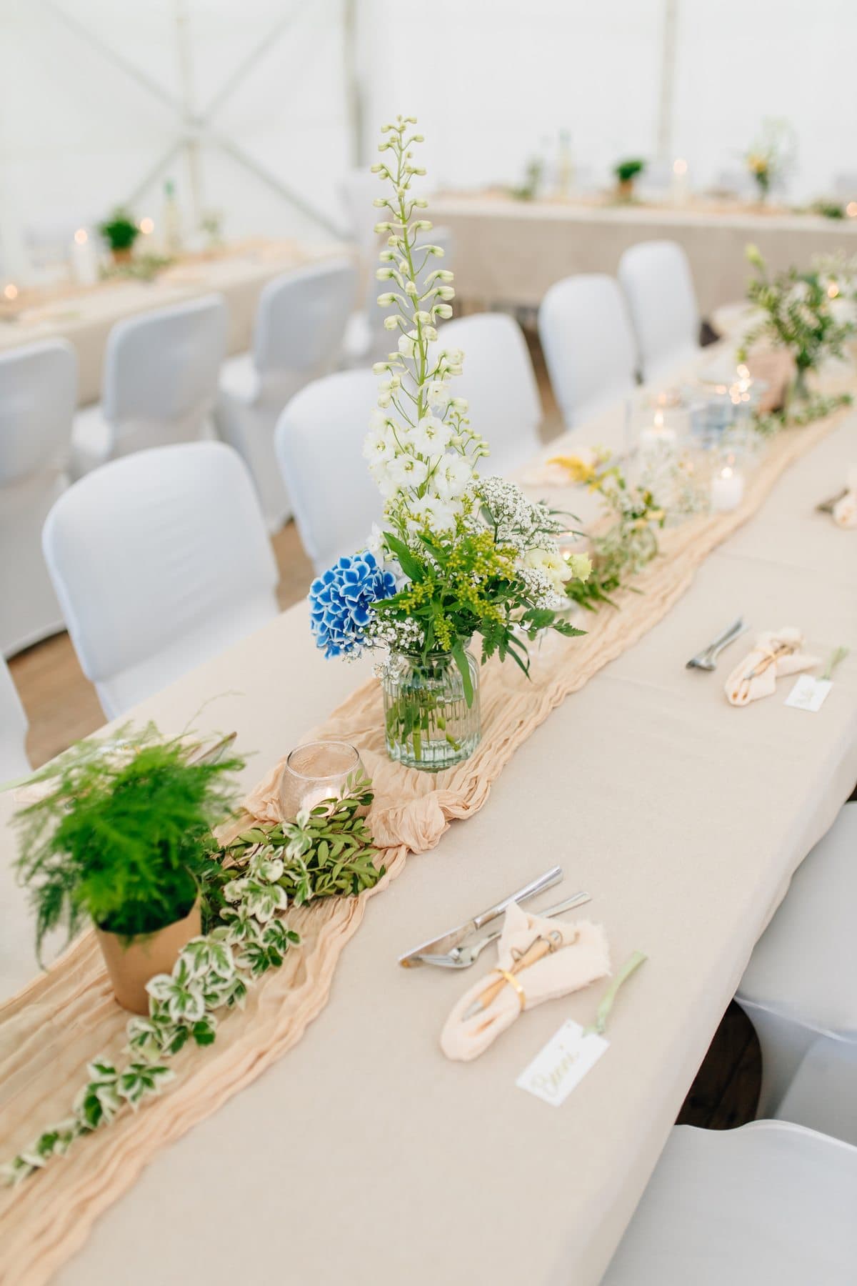 Festtafel im Zelt mit Rittersporn, blauer Hortensie, Farn, Efeu und apricotfarbenem Tischläufer