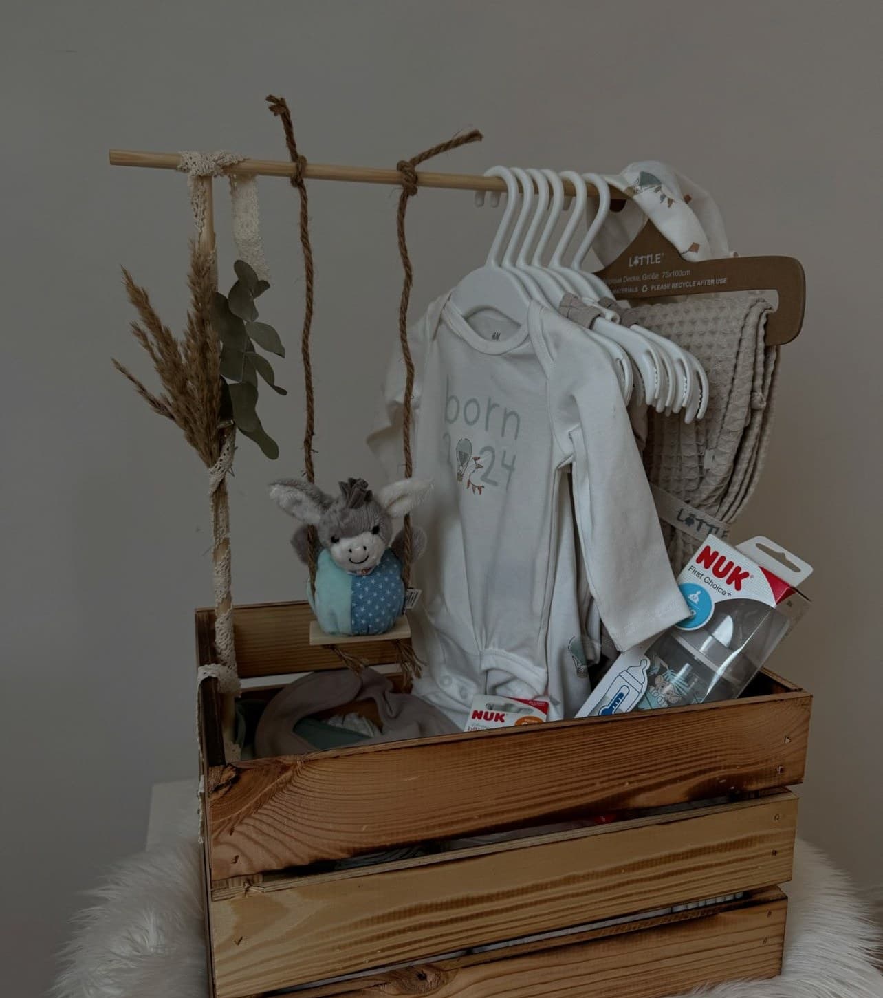 Willkommenskiste für Neugeborene: Holzkiste mit kleiner Kleiderstange, Babybody, Kuscheltier, Trockenblumen und Babyzubehör